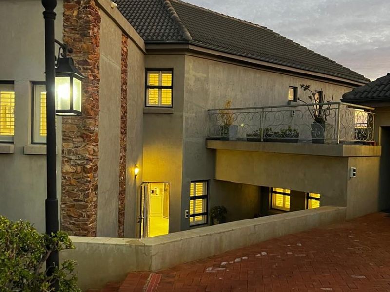 Front elevation of a multi-level residence featuring stone accents, a paved driveway, and an upper-level balcony with wrought iron railings.