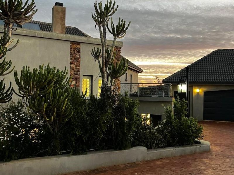Front elevation of a small holding property featuring a brick paved driveway, stone-clad accents, and a tiled roof at sunset.