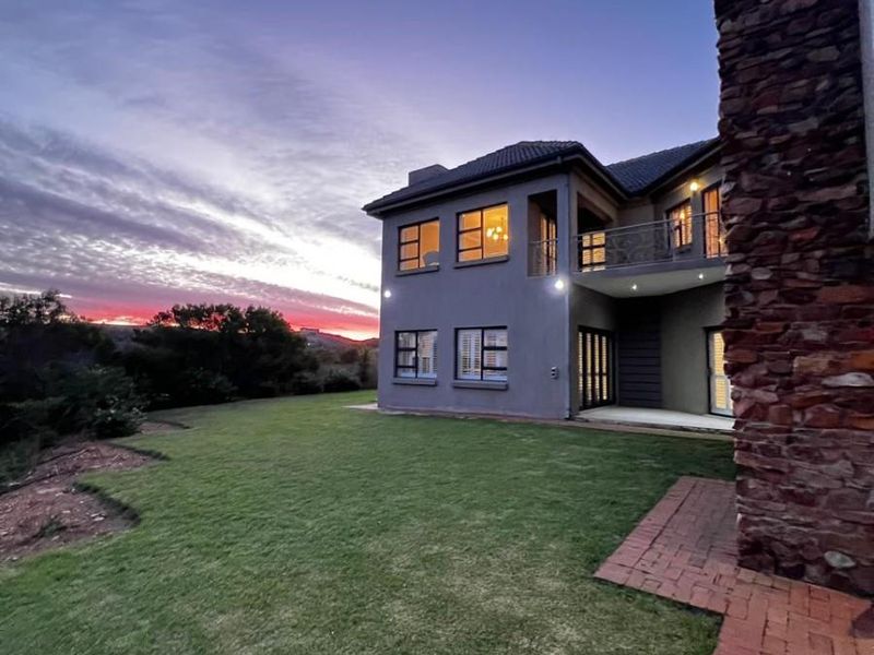 Rear view of a double-storey residence featuring stone cladding, a balcony, and a well-maintained lawn at sunset.