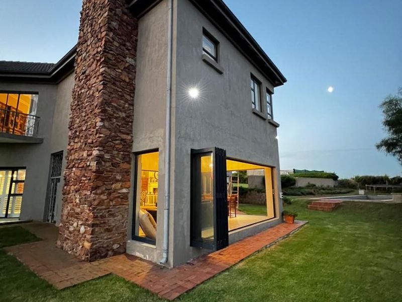Rear view of a double-story home featuring a prominent stone chimney, modern bi-fold doors opening to the garden, and brick paved pathways.