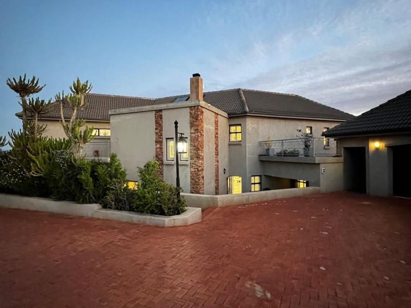 Front elevation of a multi-story residence featuring a brick paved driveway, stone-accented facade, and an upper-level balcony with wrought iron railings.