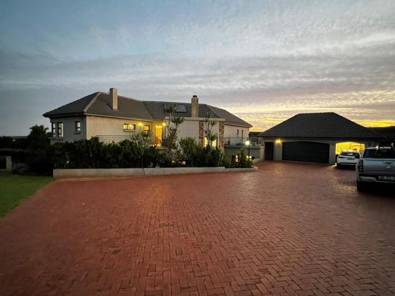 A spacious front exterior view of a small holding property featuring a large brick-paved driveway, a multi-car garage, and a well-maintained main residence.
