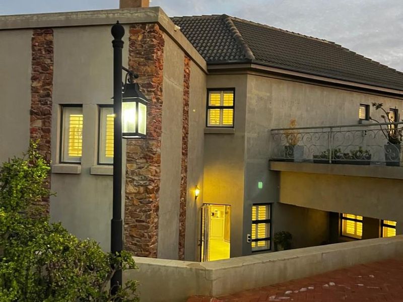 Front elevation of a multi-story home featuring stone cladding, a tiled roof, a balcony with wrought iron railings, and a brick-paved driveway.