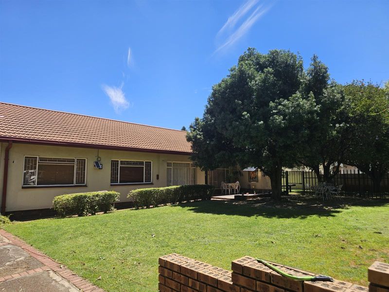 Rear view of the house featuring a well-maintained lawn, mature trees, and a paved patio area with a brick boundary wall.