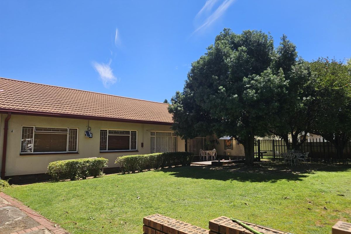 Rear view of the house featuring a well-maintained lawn, mature trees, and a paved patio area with a brick boundary wall.
