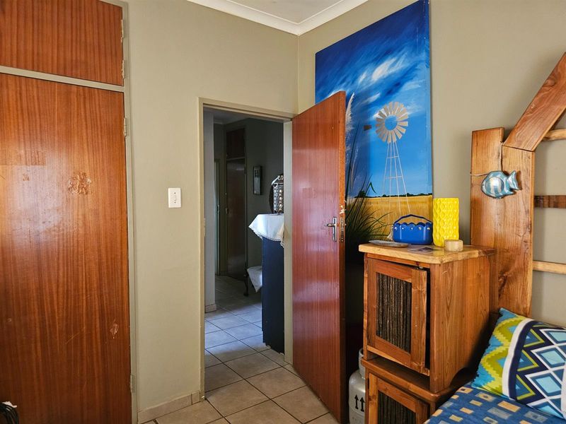 A bedroom featuring built-in wooden cupboards and tiled flooring, with a doorway leading to an adjacent hallway.