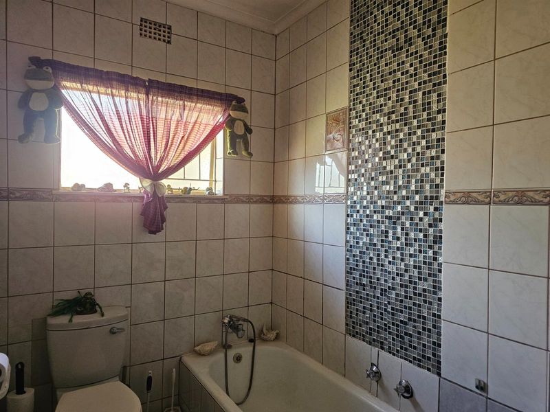 A functional bathroom featuring a built-in bathtub, toilet, and decorative mosaic tile accent wall with neutral wall tiling.