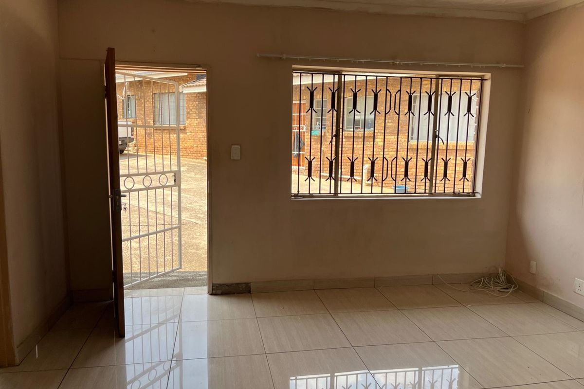 An empty living room featuring tiled flooring, a security gate at the entrance, and windows fitted with security bars.