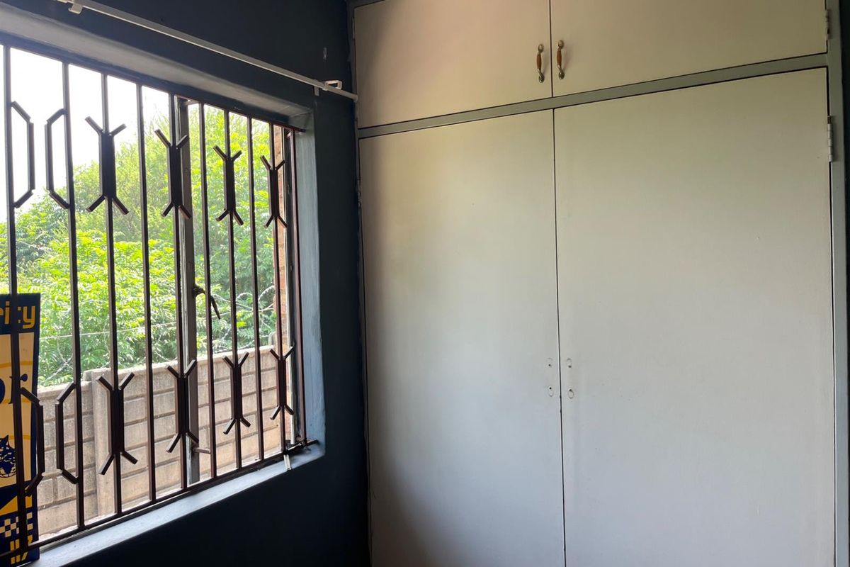 A bedroom featuring built-in cupboards and a window fitted with security bars.