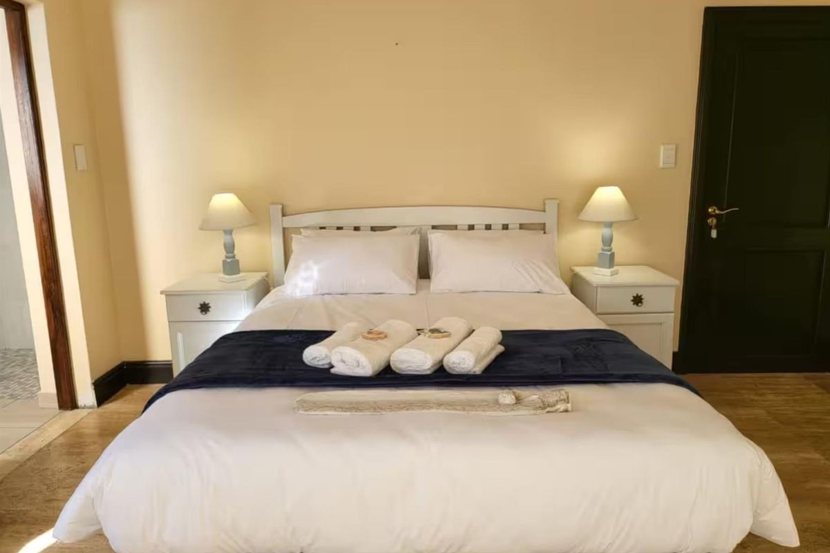 A well-lit bedroom featuring neutral wall tones, timber-look flooring, and a dark-toned interior door.
