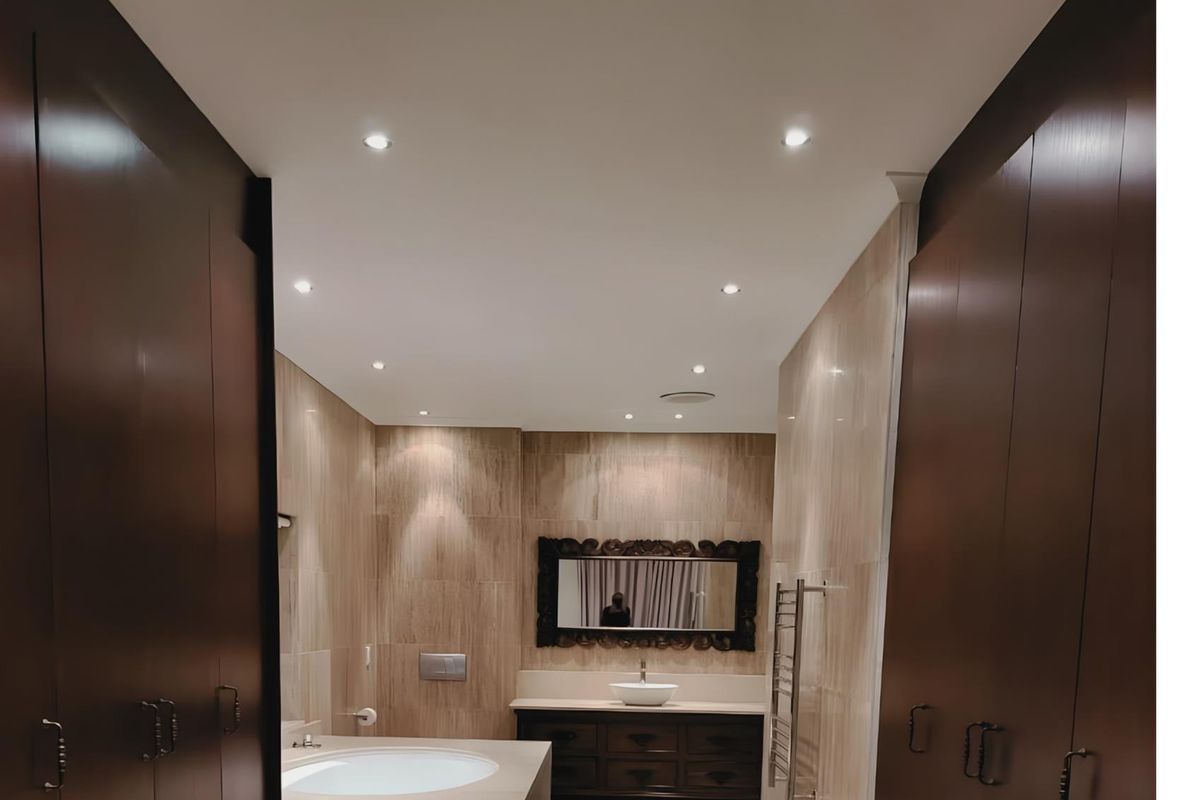 A well-appointed bathroom featuring floor-to-ceiling stone tiling, a built-in vanity with a vessel sink, a deep soaking tub, and recessed ceiling lighting.