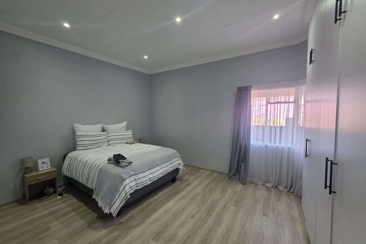 A well-maintained bedroom featuring light wood-look flooring, recessed ceiling lighting, and built-in floor-to-ceiling wardrobes.