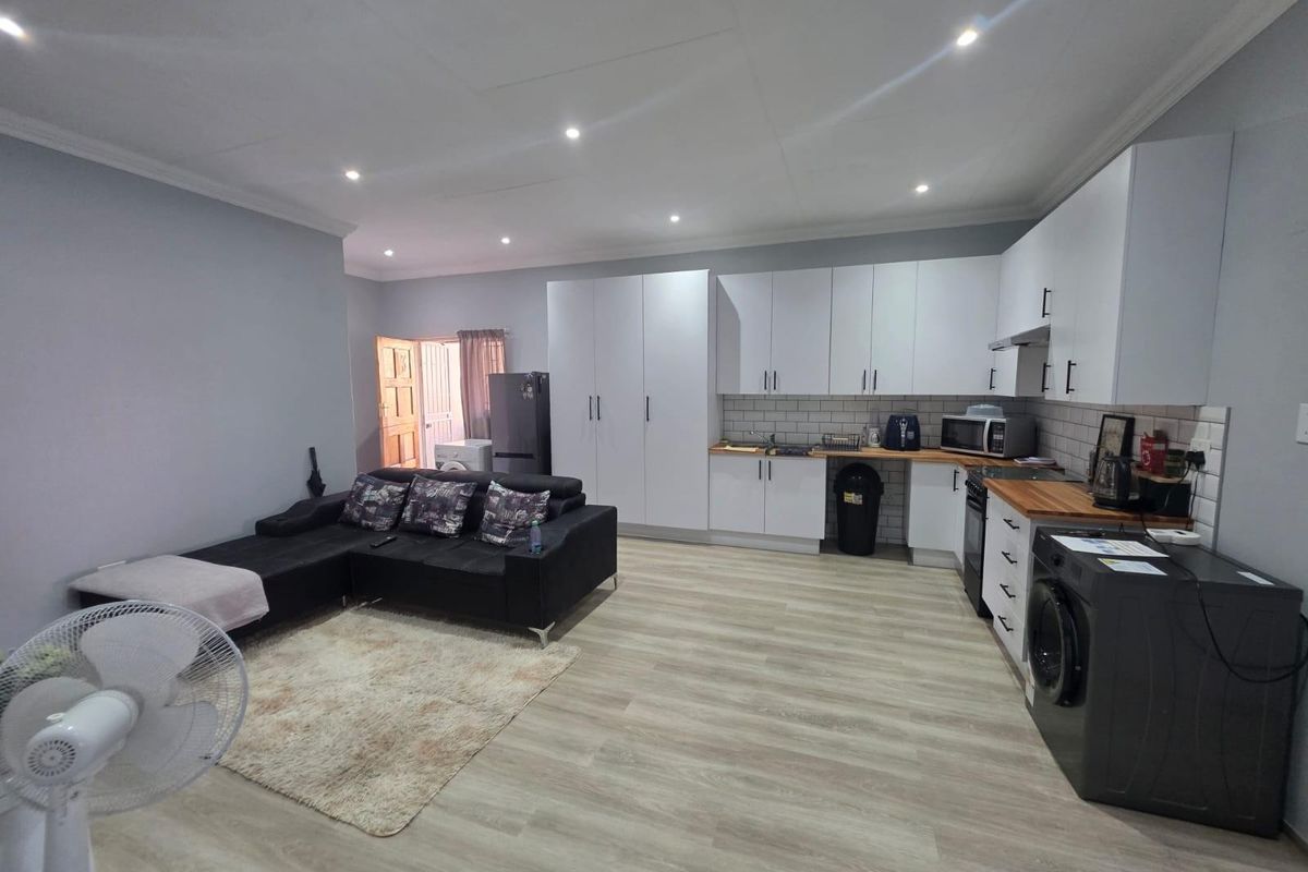 Open-plan living area featuring a modern kitchen with white cabinetry, wood countertops, subway tile backsplash, and integrated appliances, flowing into a comfortable lounge space.