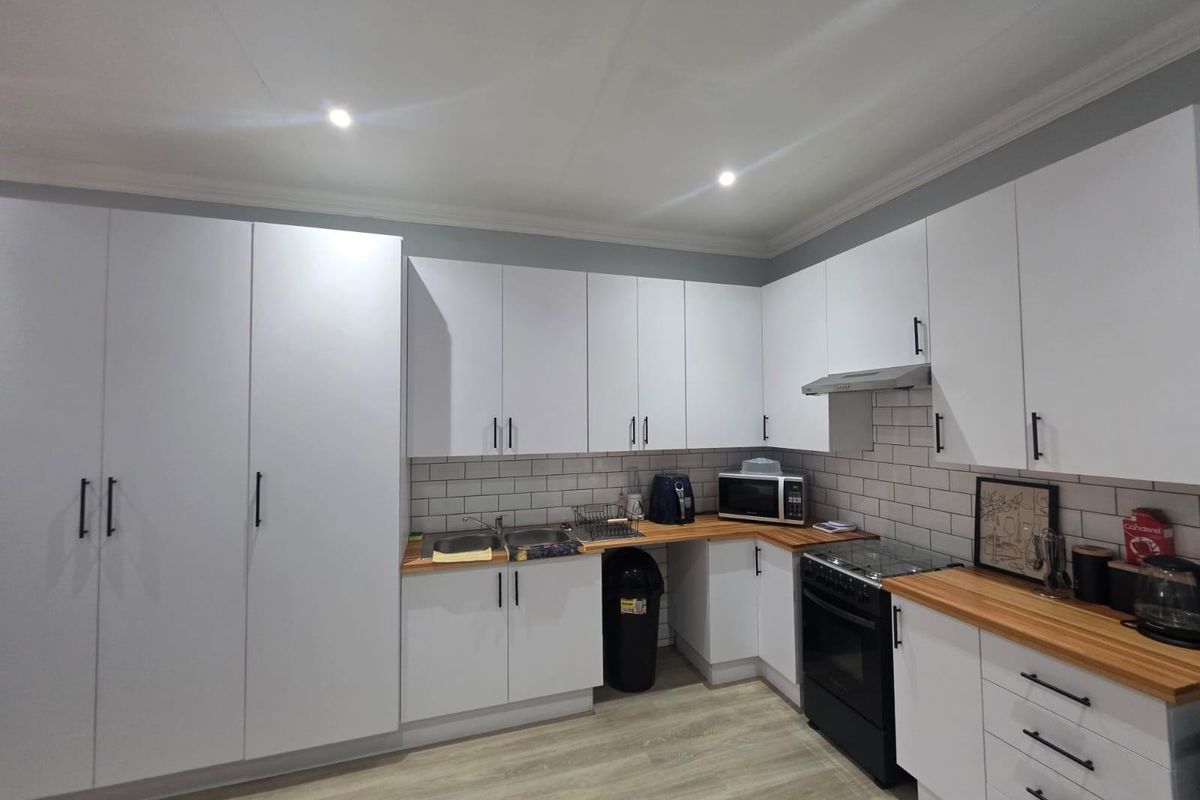 Modern kitchen featuring white cabinetry, wooden countertops, subway tile backsplash, and integrated stainless steel extractor fan.
