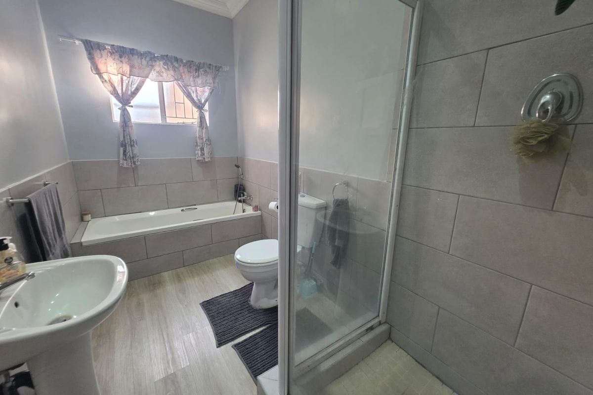 A functional bathroom featuring a separate shower enclosure, a built-in bathtub, a pedestal basin, and neutral wall tiling.