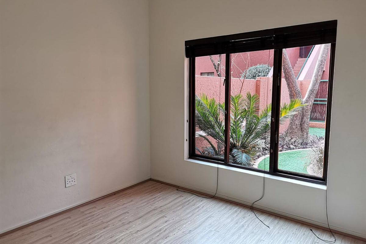 An empty bedroom featuring light wood-look laminate flooring and a large window with dark frames overlooking a private garden area.