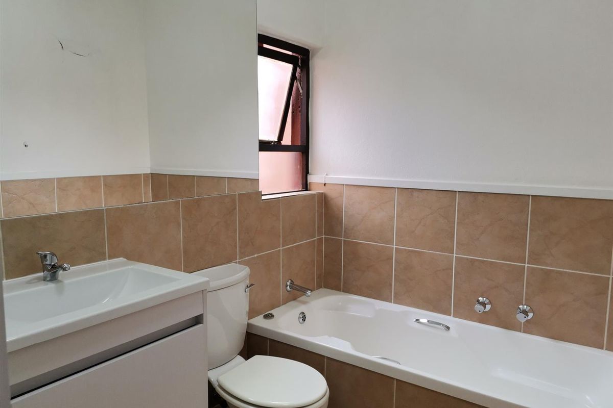 A functional bathroom featuring a built-in bathtub, vanity basin, and toilet with neutral wall tiling and a large wall-mounted mirror.