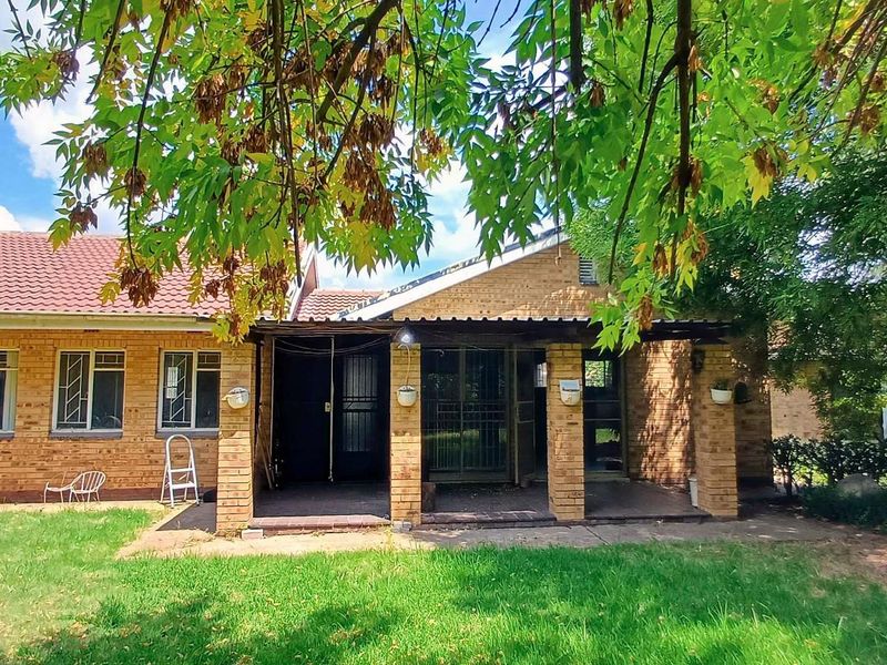 Rear view of a brick house featuring a covered patio area, tiled roof, and a spacious garden lawn.