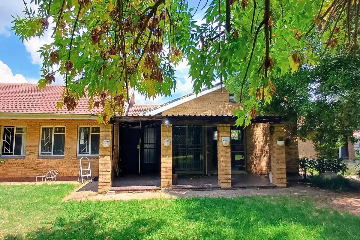 Rear view of a brick house featuring a covered patio area, tiled roof, and a spacious garden lawn.