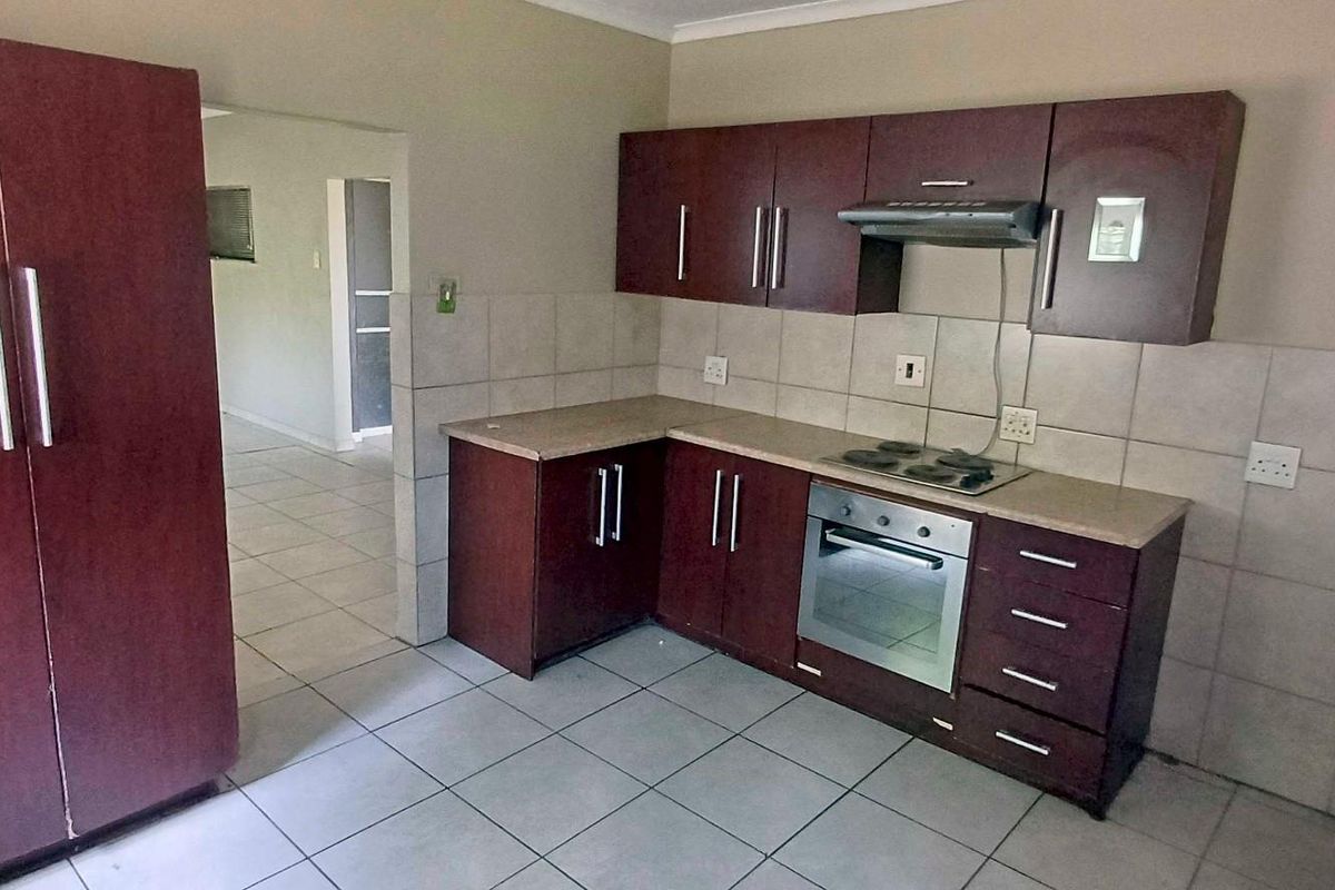 Functional kitchen featuring dark wood-finish cabinetry, laminate countertops, tiled backsplash, and integrated appliances including an oven, hob, and extractor fan.
