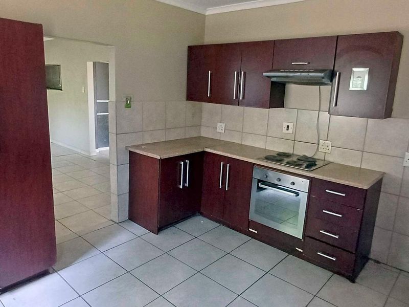 Functional kitchen featuring dark wood-finish cabinetry, laminate countertops, tiled backsplash, and integrated appliances including an oven, hob, and extractor fan.