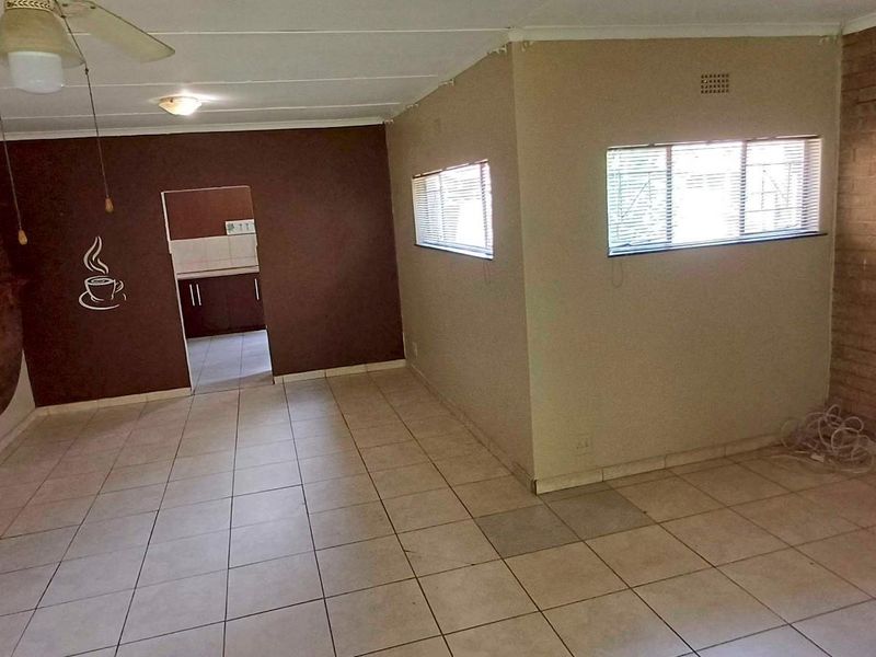 Spacious open-plan living area featuring tiled flooring, an exposed brick feature wall, and a ceiling fan, offering a versatile layout for modern living.