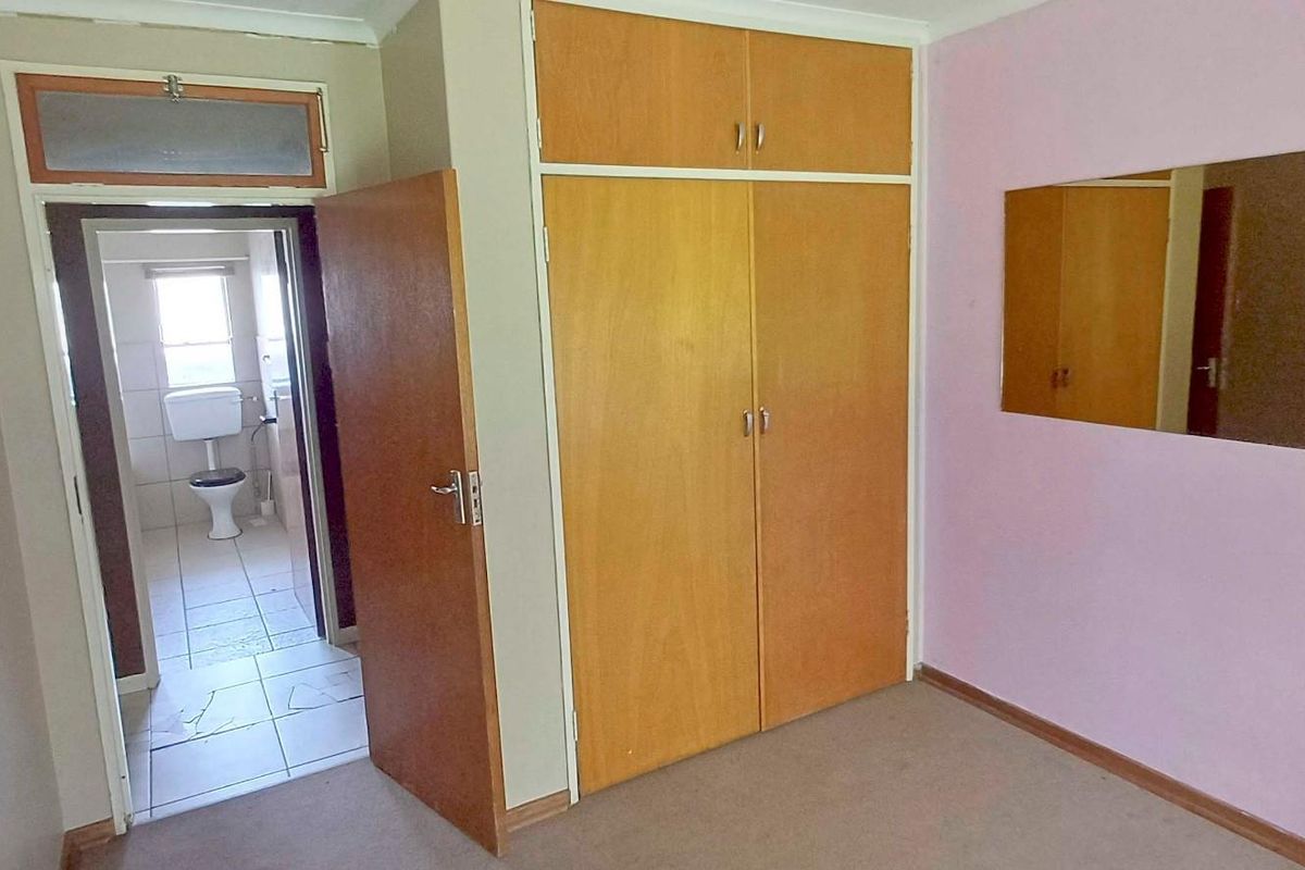 A bedroom featuring built-in wooden cupboards and direct access to an en-suite bathroom, offering a functional layout with potential for cosmetic updates.