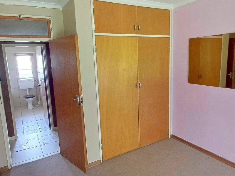 A bedroom featuring built-in wooden cupboards and direct access to an en-suite bathroom, offering a functional layout with potential for cosmetic updates.
