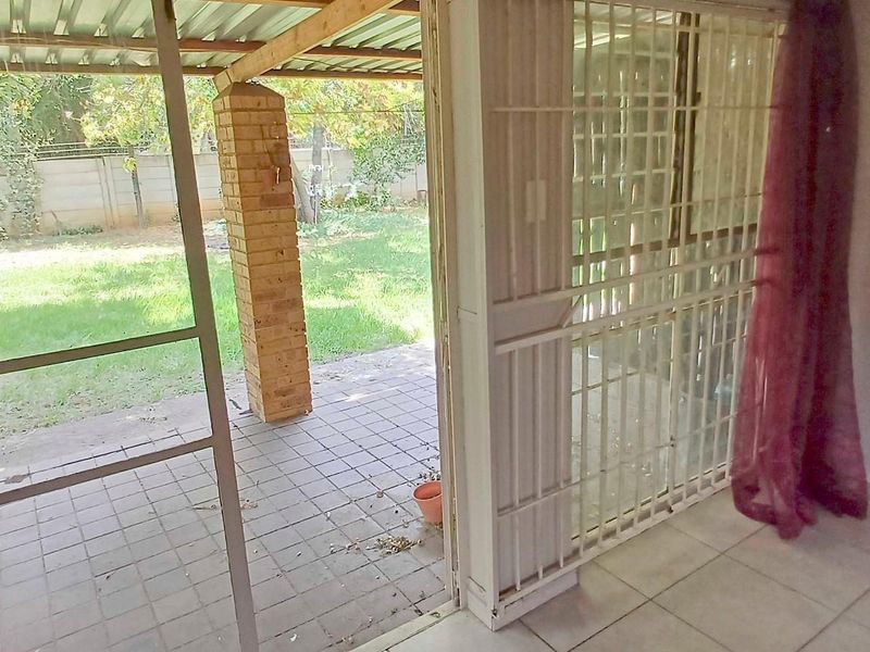 A covered outdoor patio area featuring brick pillars and tiled flooring, providing direct access to the rear garden through a sliding security door.