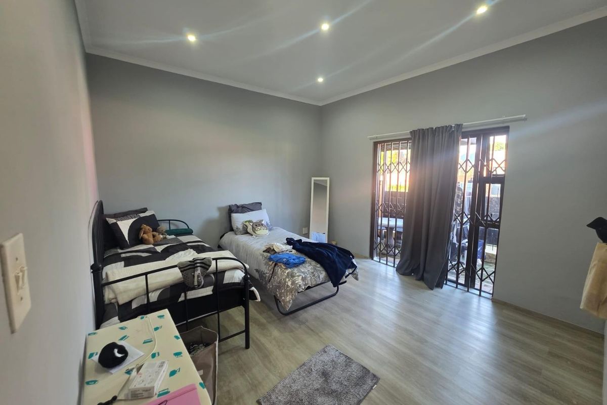 A well-lit bedroom featuring modern laminate flooring, recessed ceiling lighting, and a sliding glass door with a security gate providing access to the exterior.