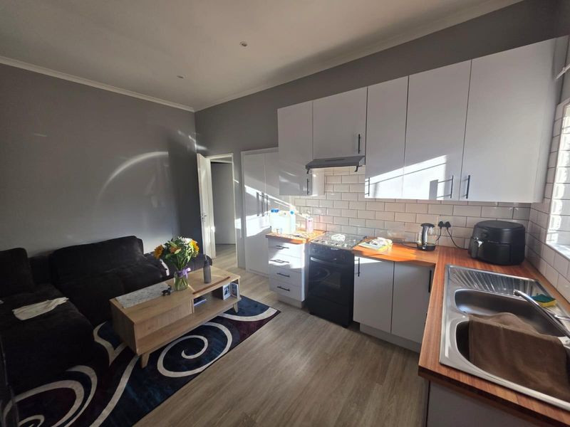 Open-plan living area featuring a modern kitchen with white cabinetry, wooden countertops, subway tile backsplash, and integrated appliances, seamlessly connected to the lounge space.