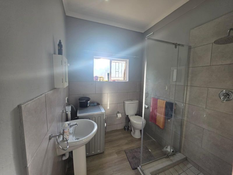A functional bathroom featuring a glass-enclosed shower, pedestal basin, and toilet with neutral wall tiling and wood-look flooring.
