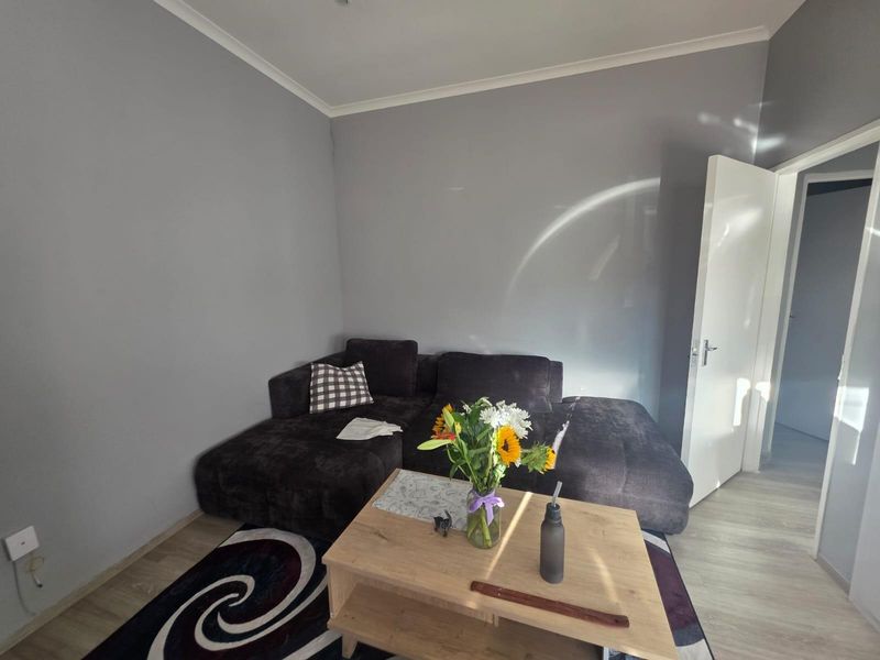 A living room featuring light-toned laminate flooring, grey painted walls, and coving, providing a neutral base for interior design.