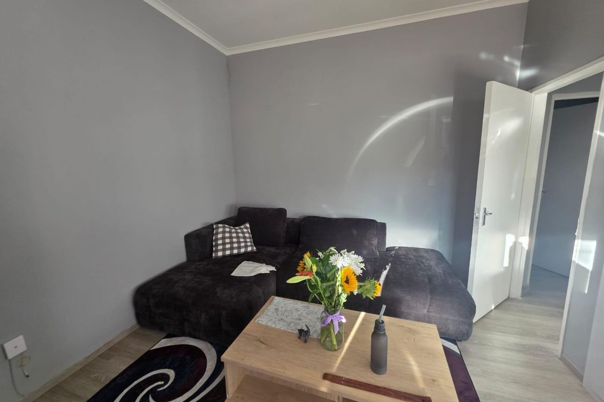 A living room featuring light-toned laminate flooring, grey painted walls, and coving, providing a neutral base for interior design.