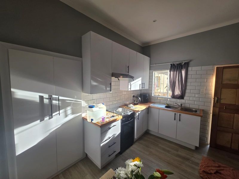 A modern kitchen featuring white cabinetry, subway tile backsplash, wooden countertops, and a stainless steel sink, complemented by laminate flooring.