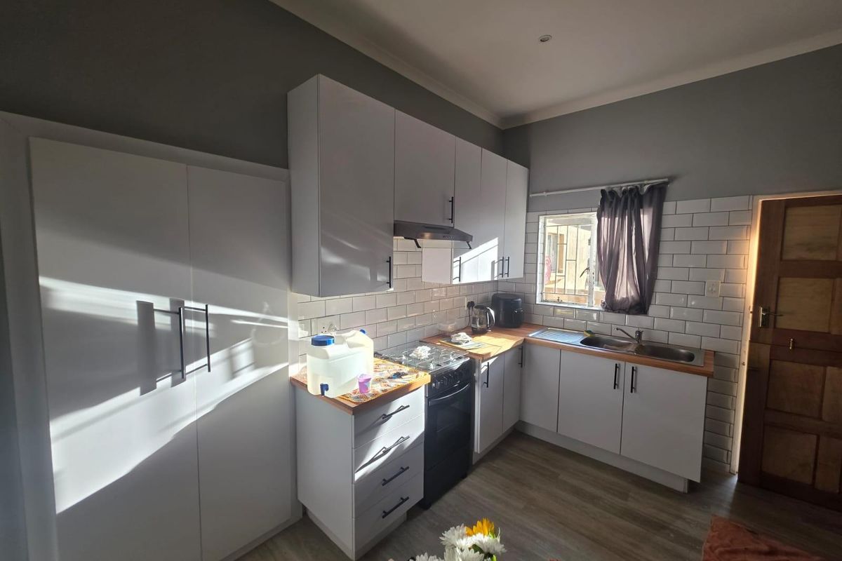 A modern kitchen featuring white cabinetry, subway tile backsplash, wooden countertops, and a stainless steel sink, complemented by laminate flooring.