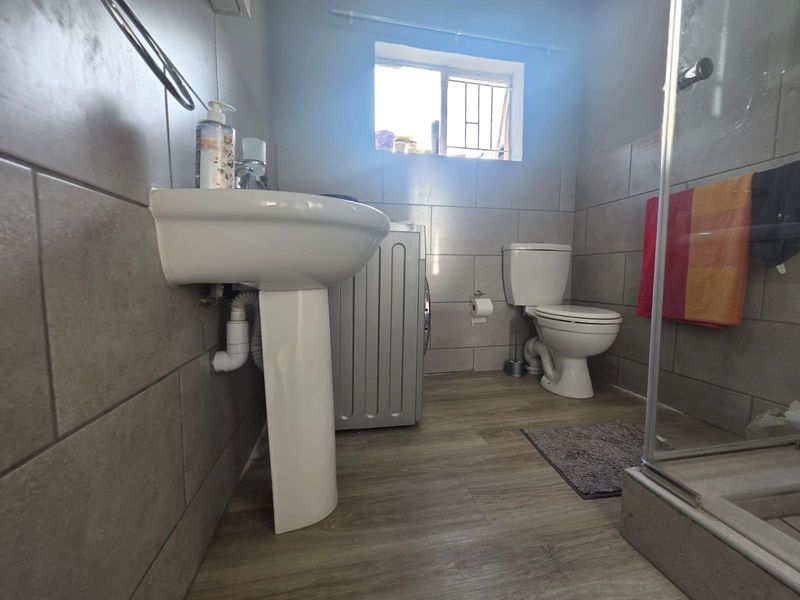 A functional bathroom featuring a pedestal washbasin, toilet, and shower enclosure with neutral wall tiling and wood-look laminate flooring.