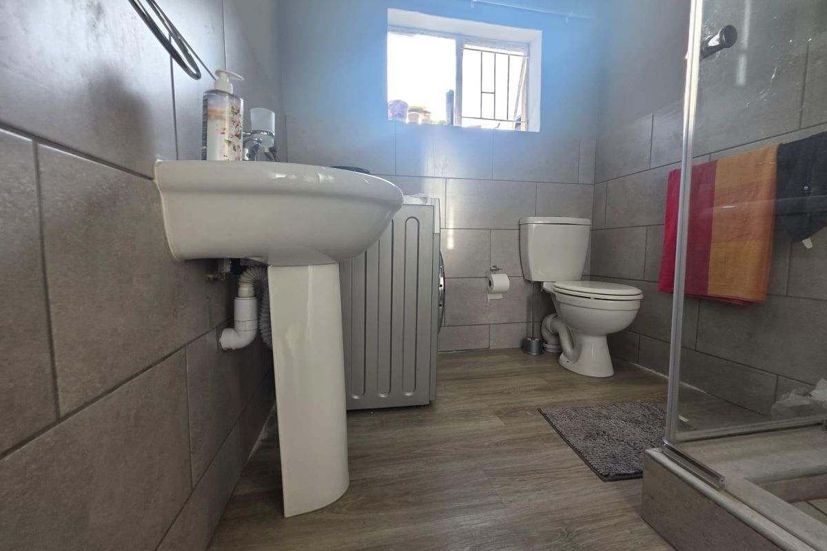 A functional bathroom featuring a pedestal washbasin, toilet, and shower enclosure with neutral wall tiling and wood-look laminate flooring.