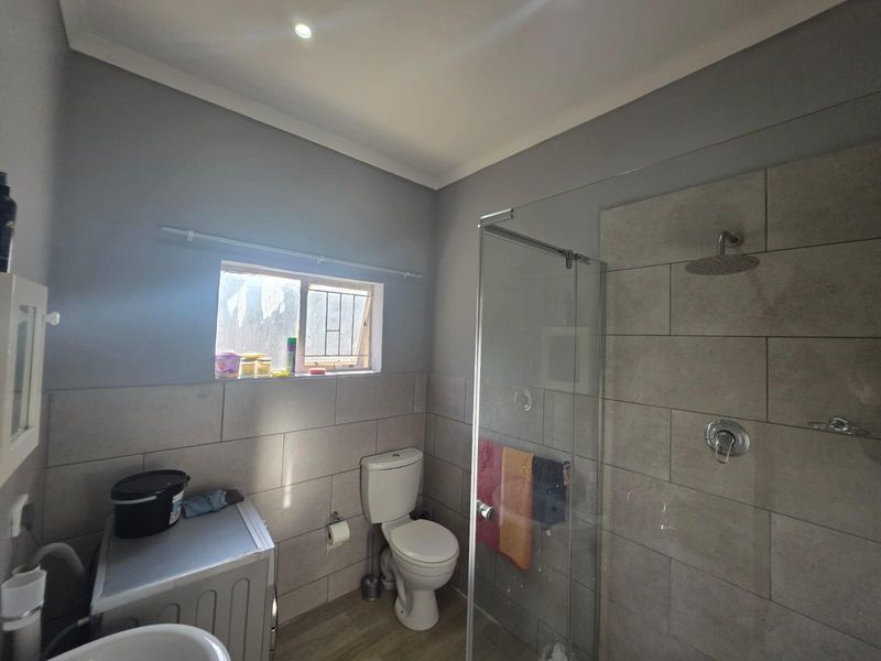 A modern bathroom featuring a glass-enclosed shower with a rain shower head, a toilet, and neutral-toned wall tiling.