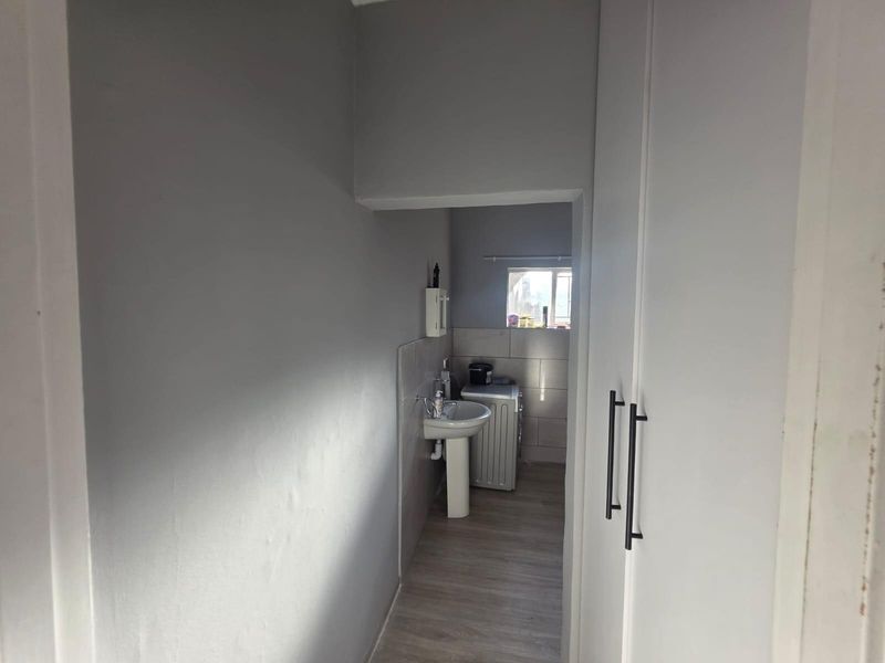 A functional laundry area featuring a pedestal sink, tiled splashback, and built-in storage cabinetry, providing a clean and practical utility space.