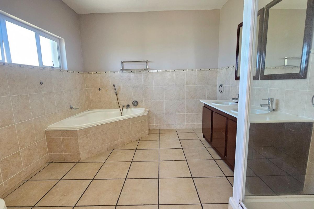 Spacious bathroom featuring a corner bathtub, double vanity with dark wood cabinetry, and tiled flooring and walls.