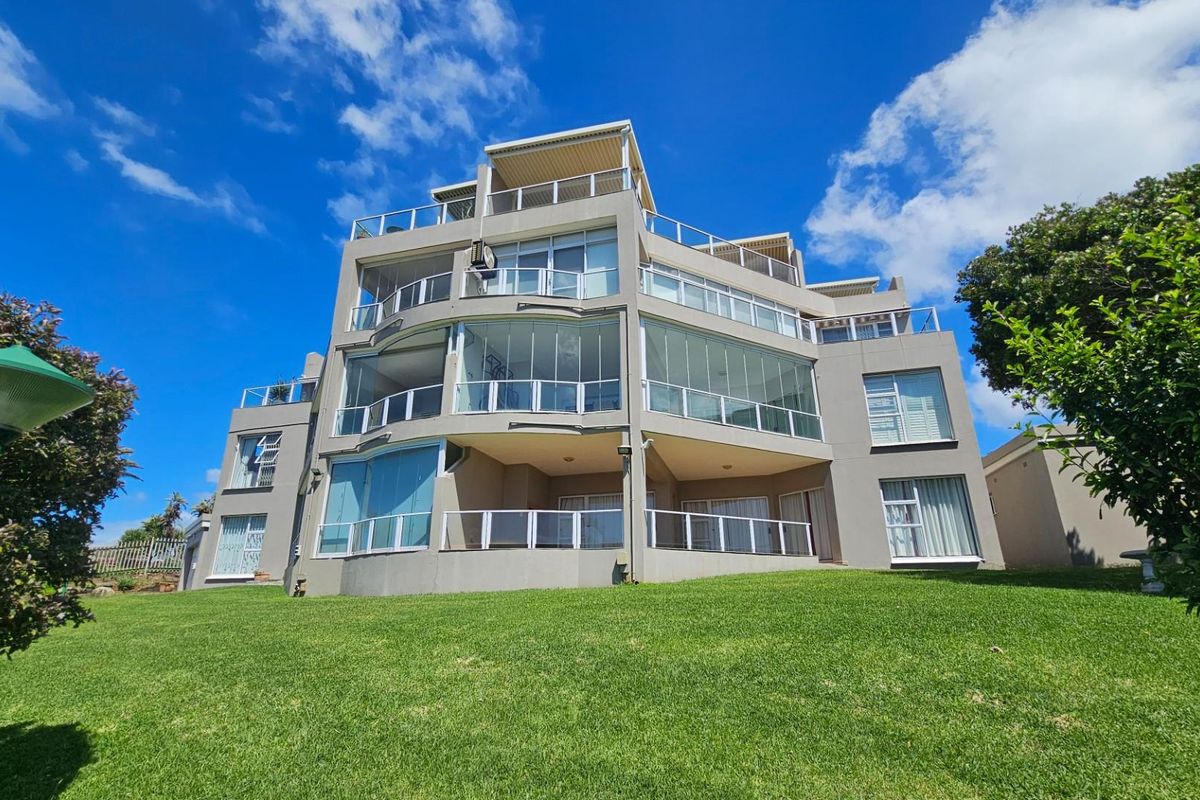 A multi-story apartment building featuring glass-enclosed balconies, modern architectural design, and well-maintained exterior finishes set against a clear blue sky.