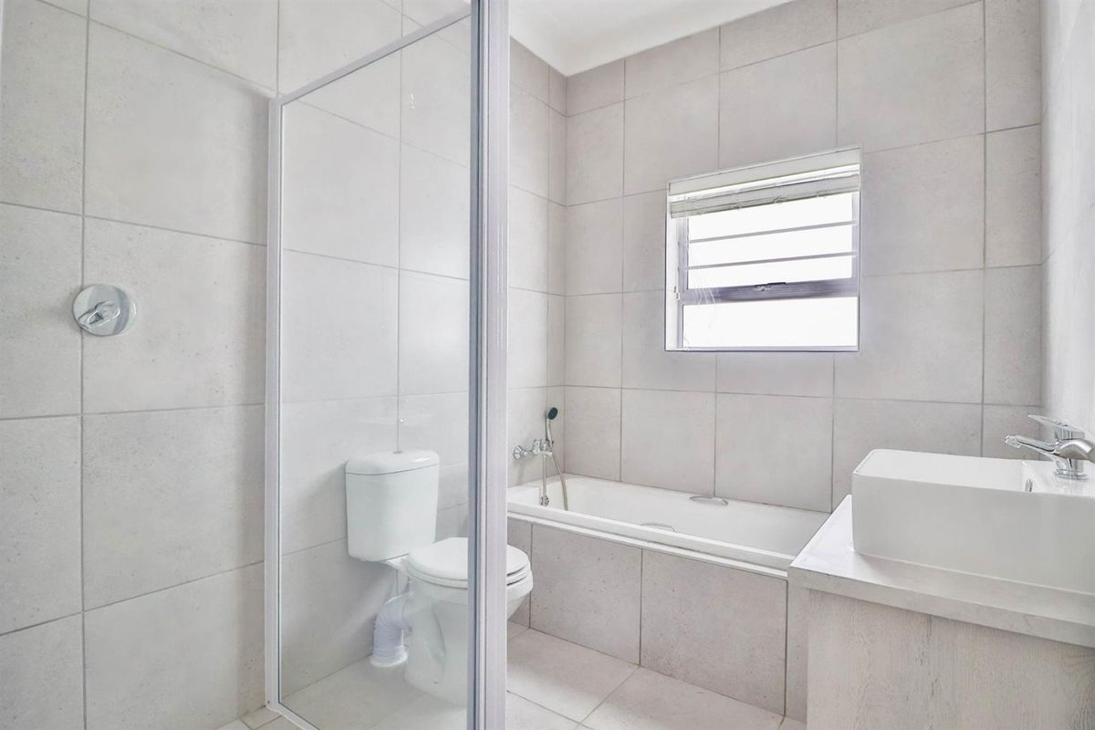 Modern bathroom featuring neutral floor-to-ceiling tiling, a glass-enclosed shower, a built-in bathtub, and a contemporary vanity basin.