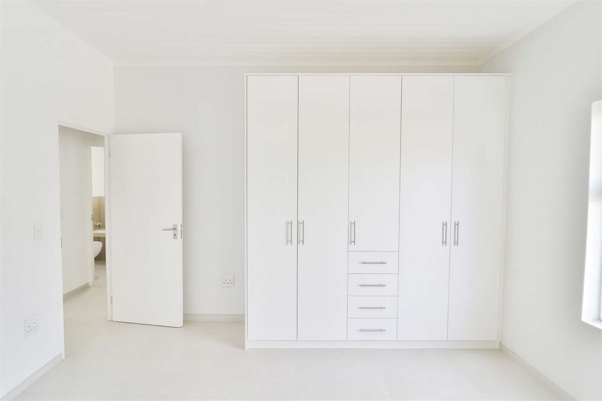 A bright, minimalist bedroom featuring built-in white cabinetry with integrated drawers and a doorway leading to an adjacent bathroom.