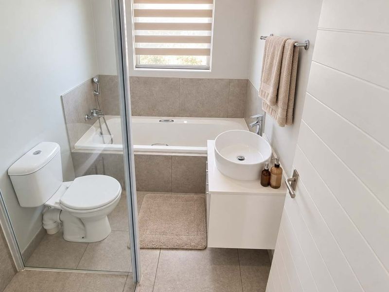 Modern bathroom featuring a built-in bathtub, vessel sink on a wall-mounted vanity, toilet, and neutral tiled finishes.