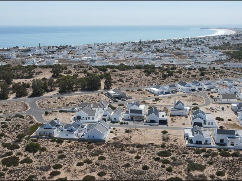 An aerial view of a coastal residential estate featuring white houses with dark roofs, situated near the ocean.