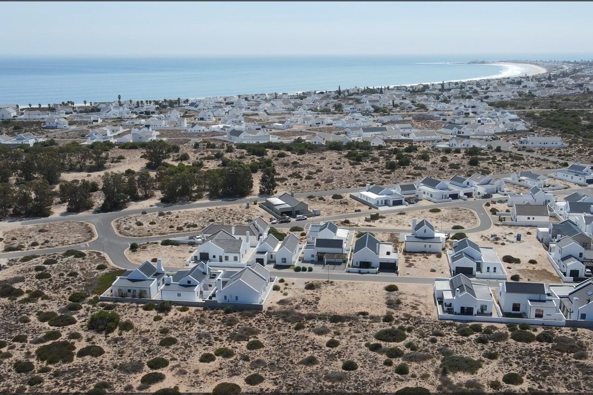 An aerial view of a coastal residential estate featuring white houses with dark roofs, situated near the ocean.
