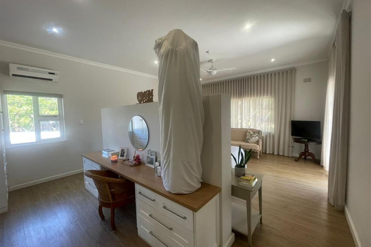 Spacious bedroom featuring a central partition wall with built-in vanity cabinetry, wood-look flooring, recessed lighting, and a wall-mounted air conditioning unit.
