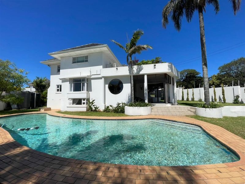 A well-maintained two-story residence featuring a curved swimming pool, landscaped garden, and a covered patio area.