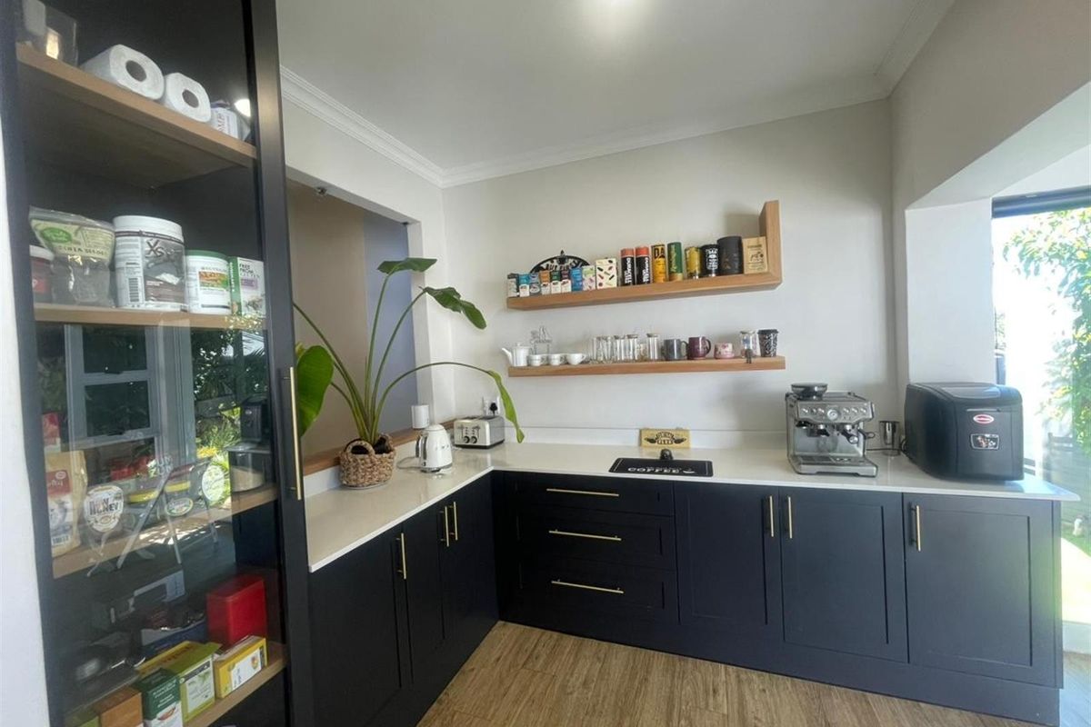 Modern kitchen featuring dark cabinetry, light stone countertops, floating timber shelves, and wood-look flooring, creating a clean and contemporary culinary space.